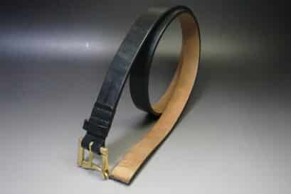 Black leather belt with a gold buckle lying in a curved arc on a gray gradient background.