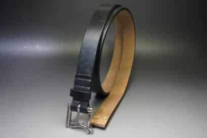 Black leather belt with a silver buckle lying on a neutral surface, showing the dark exterior and tan interior.