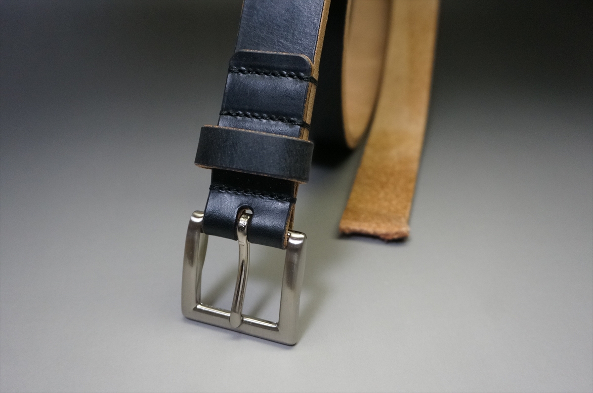 Close-up of a dark blue leather belt with a silver metal buckle on a gray surface.