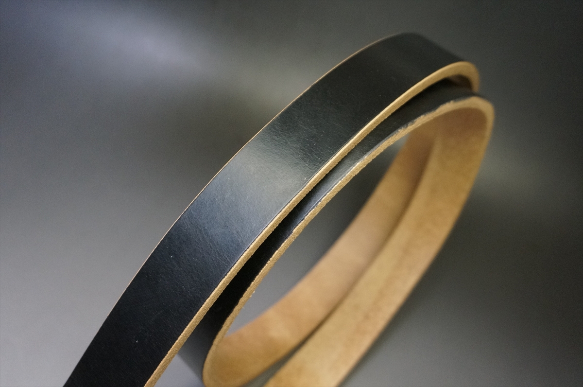 Close-up of a black leather belt with a natural brown inner side showing where it’s cut and finished.