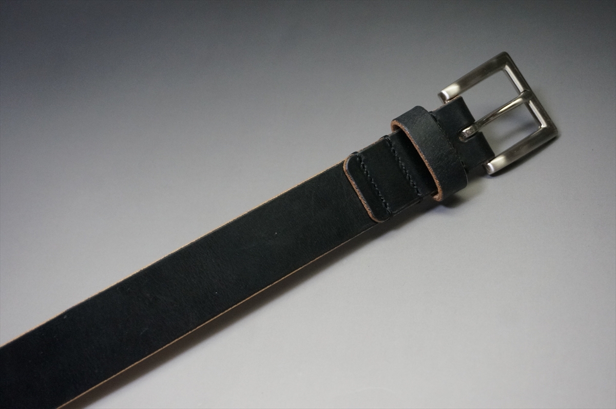 Black leather belt with a metal silver buckle photographed on a gray gradient background.
