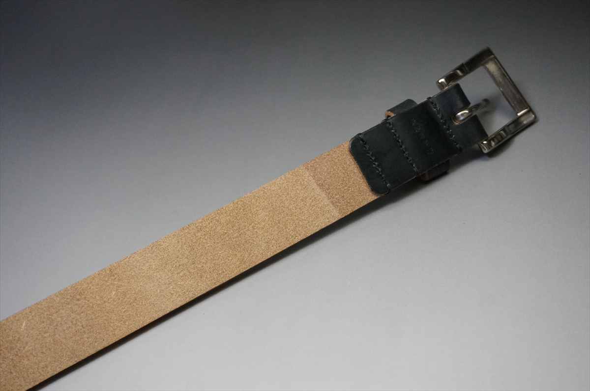 Tan suede belt with a black leather keeper and metal buckle laid diagonally on a gray surface (fashion accessory)