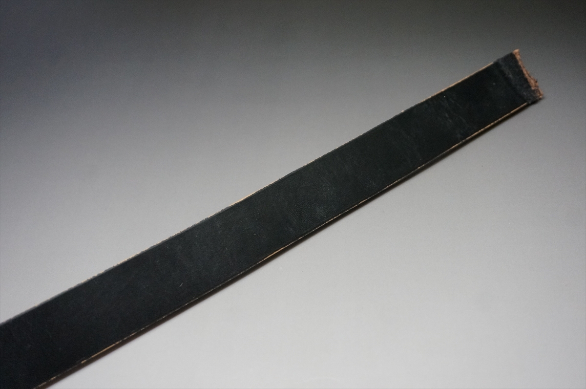 Long black abrasive strip (sanding belt) laid diagonally on a gradient background, showing a rough brown edge at one end.