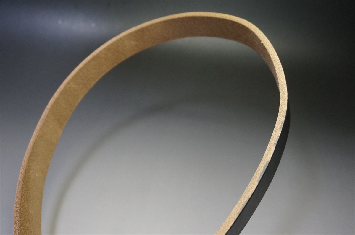 Close-up of a curved light-brown leather strip forming a partial ring against a dark gradient background.