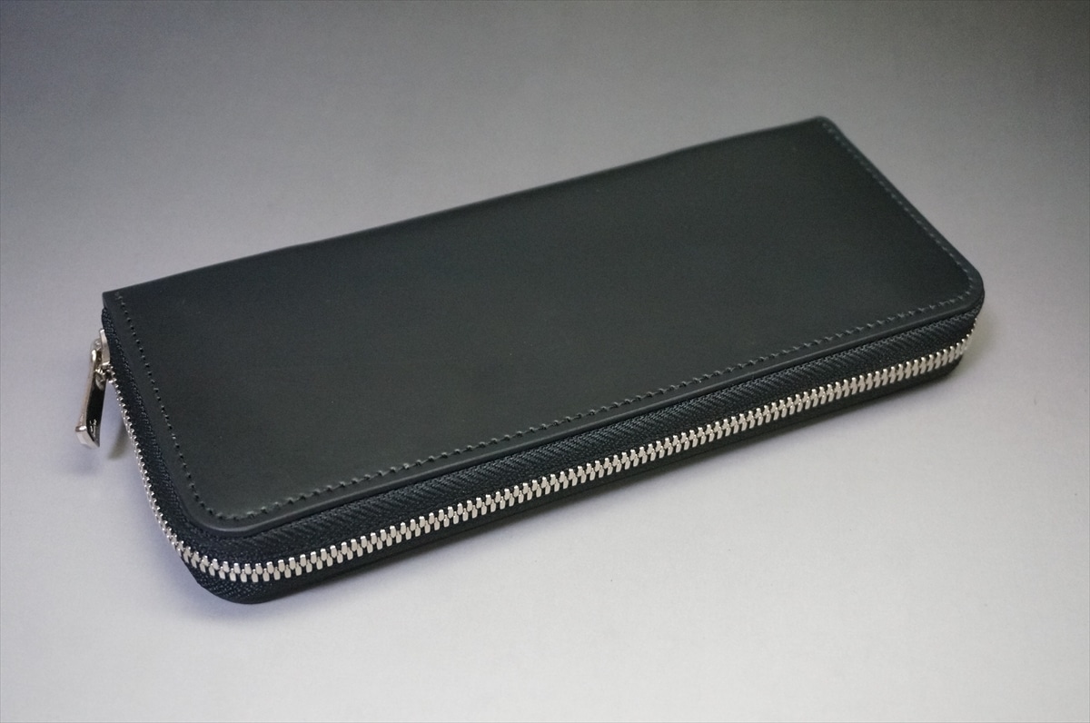 Black zippered leather wallet on a neutral surface, closed with visible silver zipper teeth and neat stitching