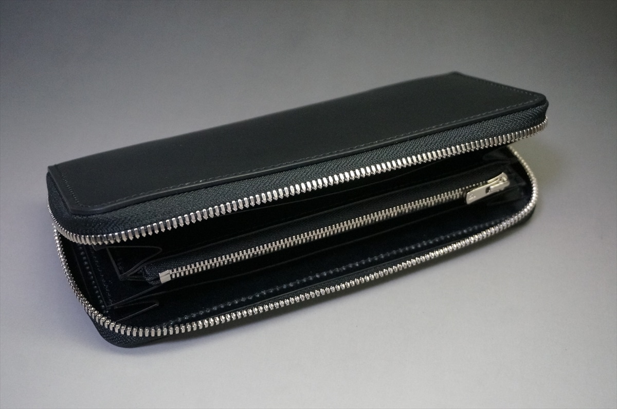 Black leather zippered wallet opened to reveal multiple card slots and a central coin zipper pouch on a gray surface.