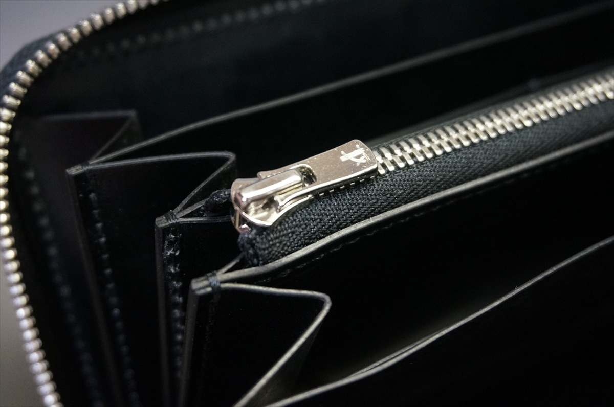 Close-up of a silver zipper on a black fabric wallet, open to reveal inner compartments.