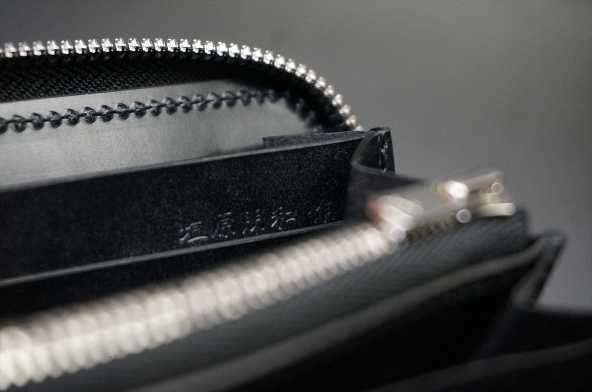 Close-up of overlapping silver zipper teeth on a dark black leather bag, showing fine stitching and texture.