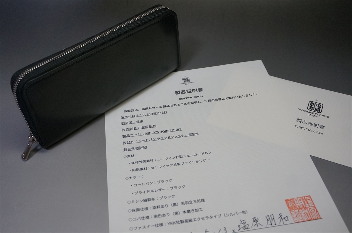 Black zippered leather wallet resting beside Japanese certification documents with red seal stamps on a gray surface.",