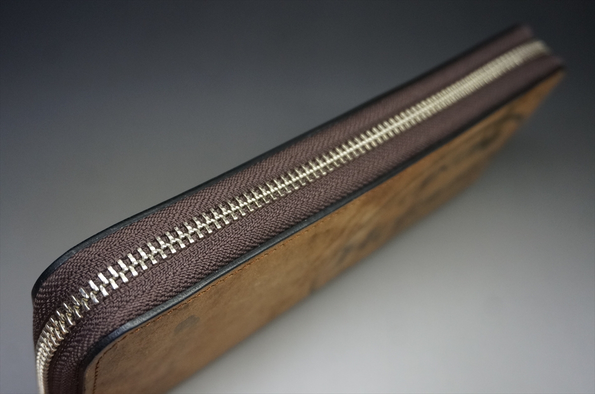 Close-up of a brown leather zipper wallet with silver teeth along the edge.