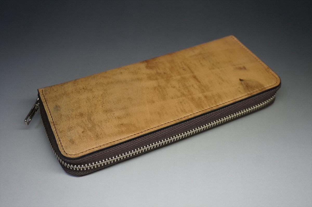 Brown leather zippered wallet resting on a gray surface, angled to show the zipper edge.