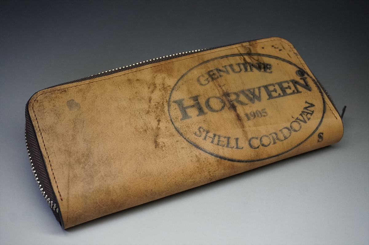 Brown leather zippered wallet with a circular stamp reading 'Genuine Horween Shell Cordovan' on a gray background.