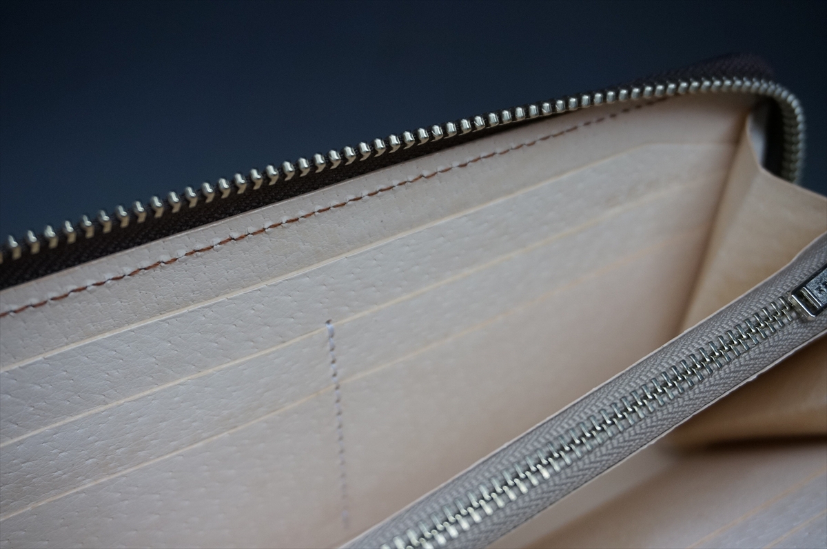 Close-up of a beige leather wallet interior showing card slots and a silver zipper edge.