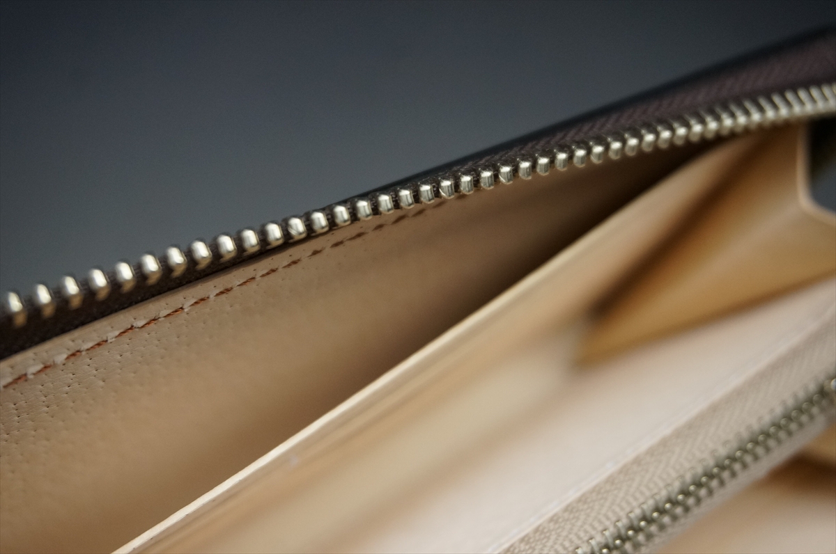 Close-up of a beige leather wallet interior with a metal zipper running along the top edge.