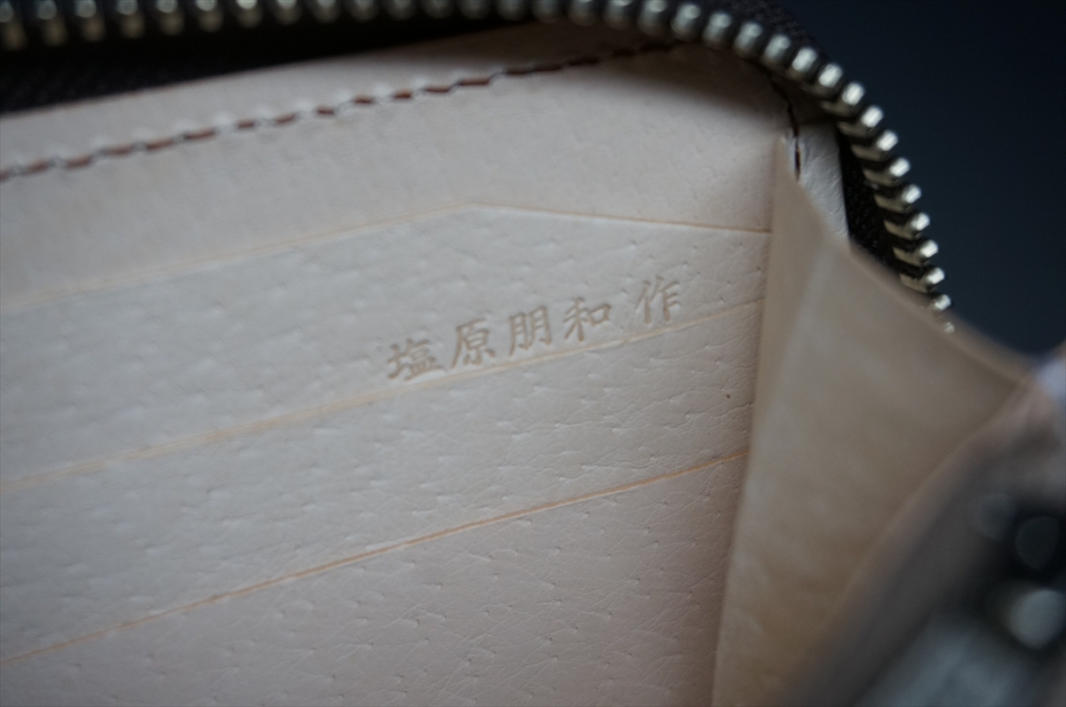 Inside of a light beige wallet/purse showing stitched seams and a stamped maker's signature in Japanese characters on the inner lining