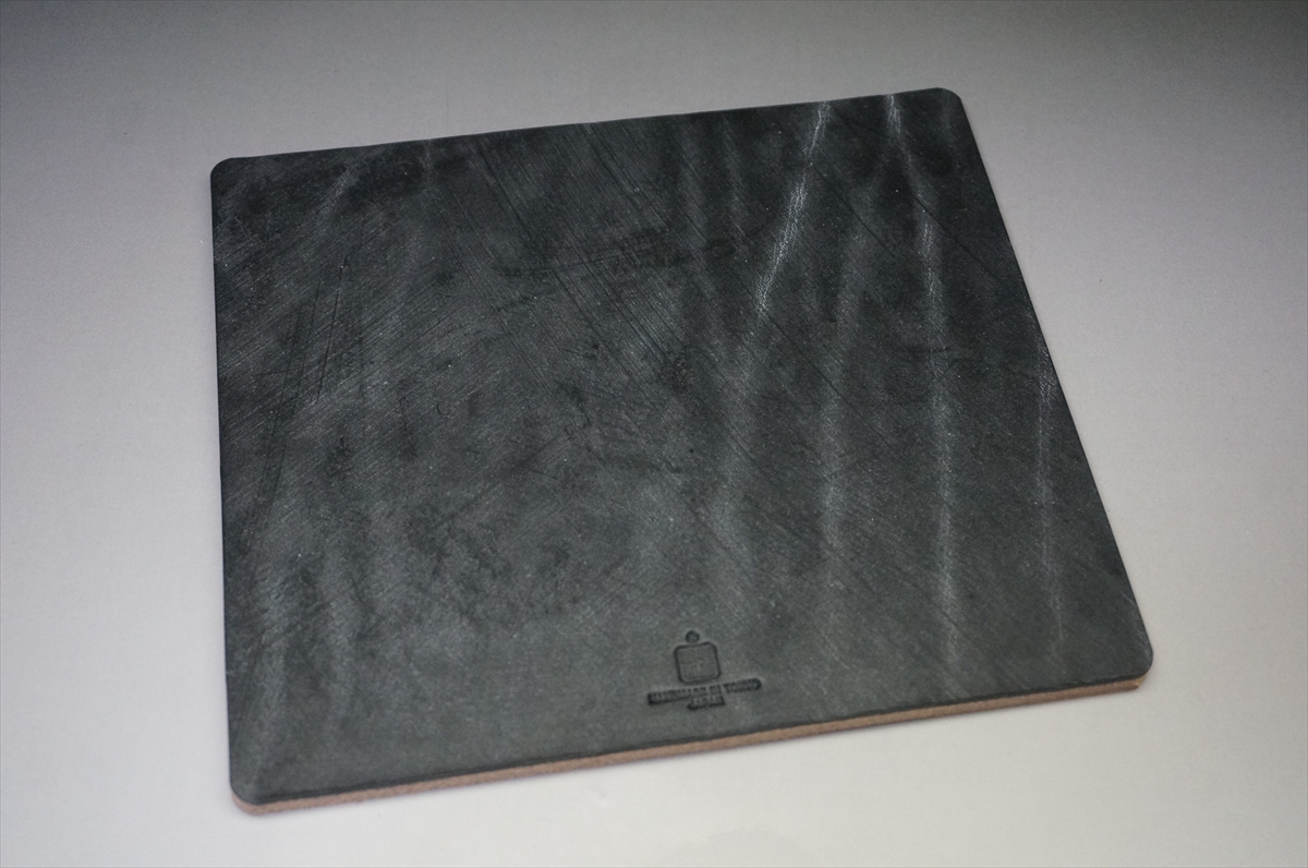 Slate square serving board with rounded corners and a small brand stamp near the bottom edge (textured, charcoal-gray surface).