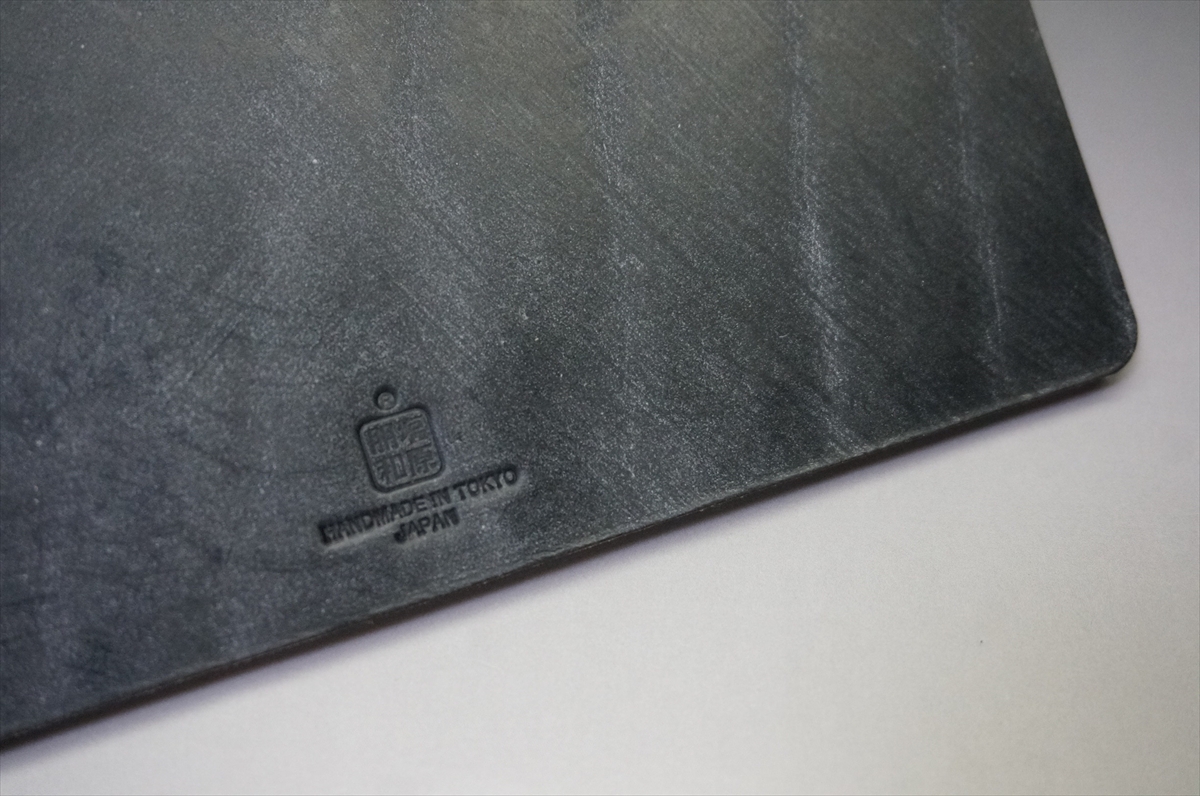 Close-up of a dark, textured surface with a small embossed stamp reading 'HANDMADE IN TOKYO JAPAN'.