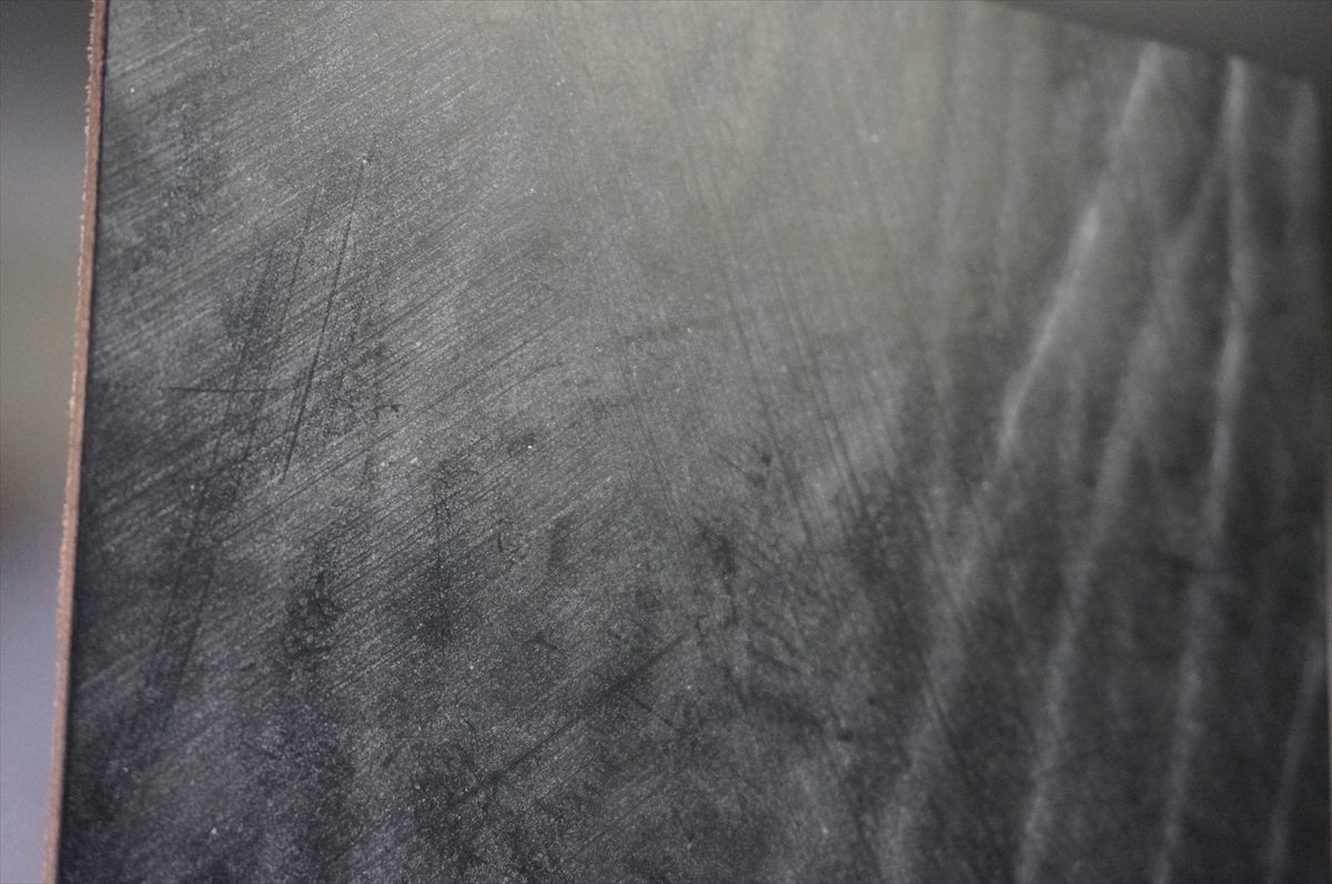 Close-up of a dark, scratched metal surface with prominent scuffs and marks.