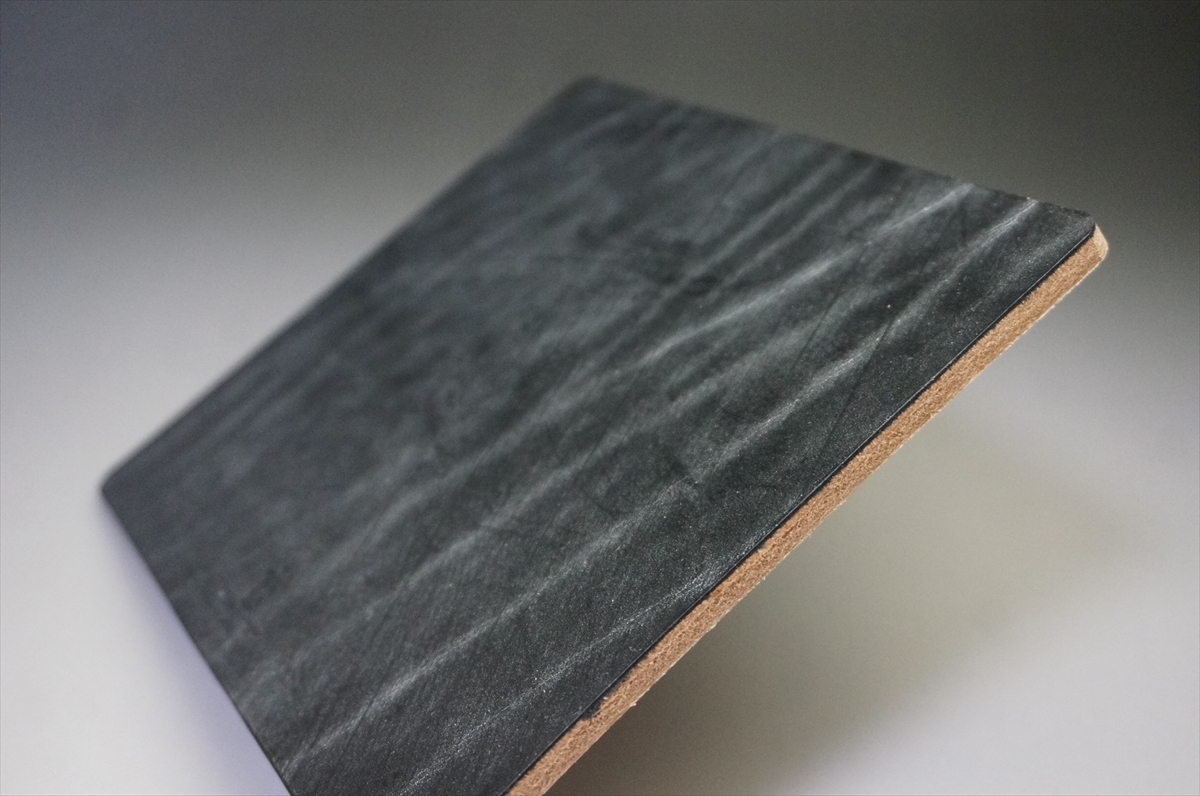Close-up of a dark slate tile with a cork-backed edge, angled on a light surface.