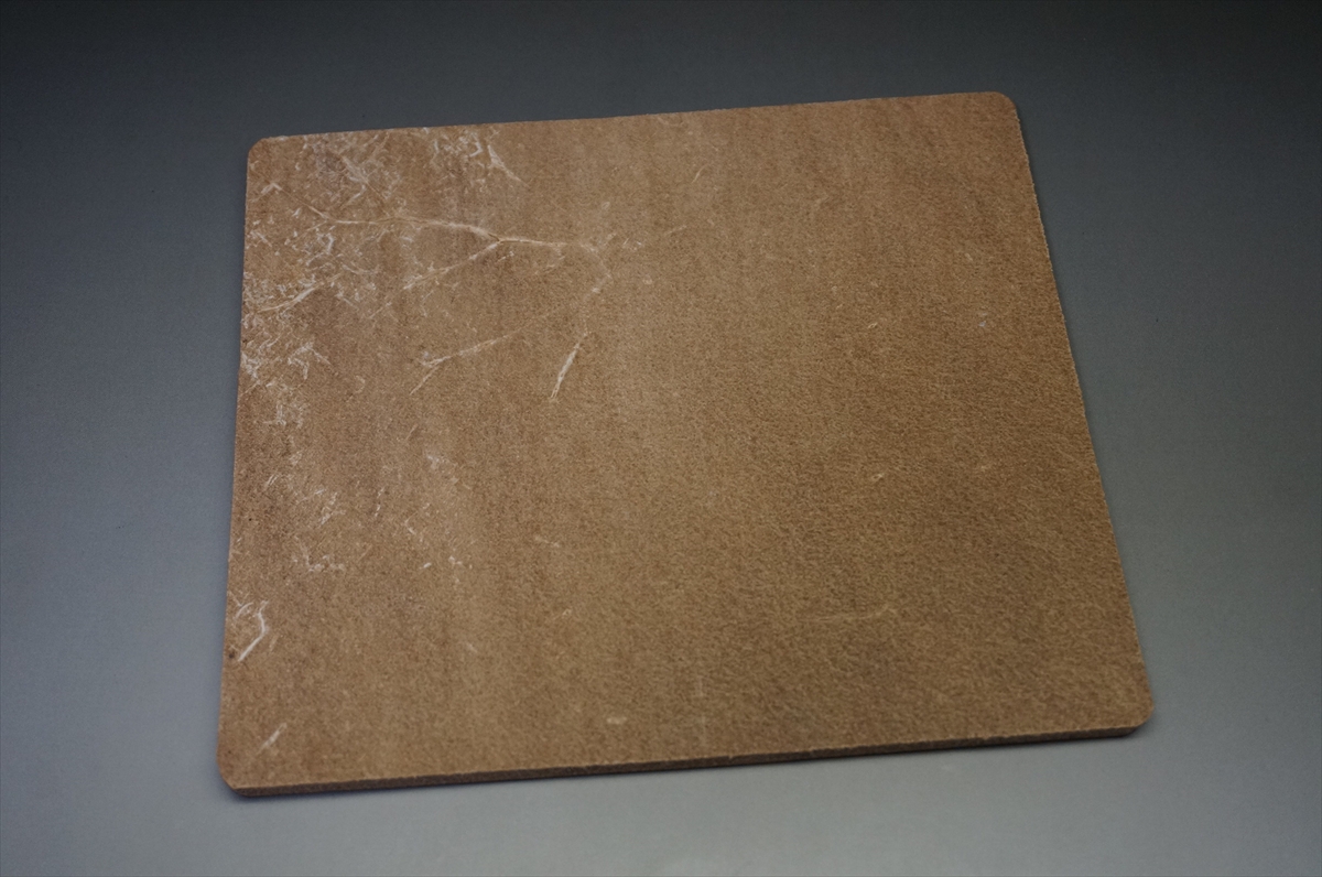 Brown corkboard tile with rounded corners resting on a gray surface.