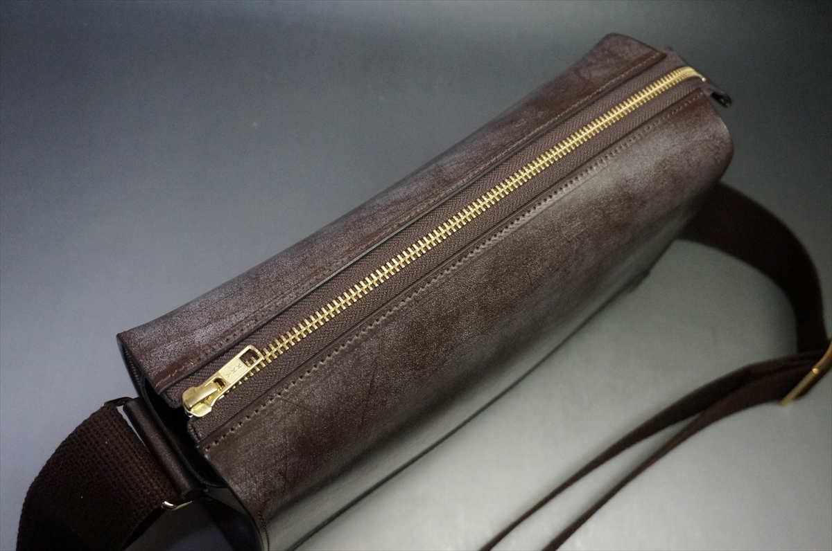 Brown leather crossbody bag with a gold zipper along the top, shown from the side edge.