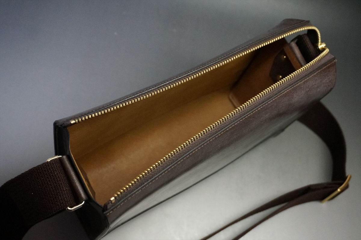 Brown leather zippered shoulder bag opened to show a tan interior and gold zipper. The strap is attached on the side edge.