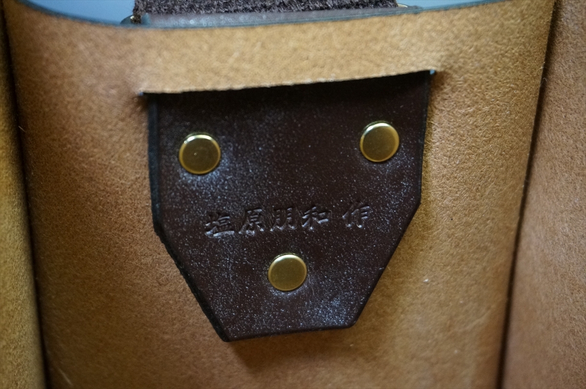 Close-up of a brown leather piece with three brass rivets and embossed Japanese characters in the center.