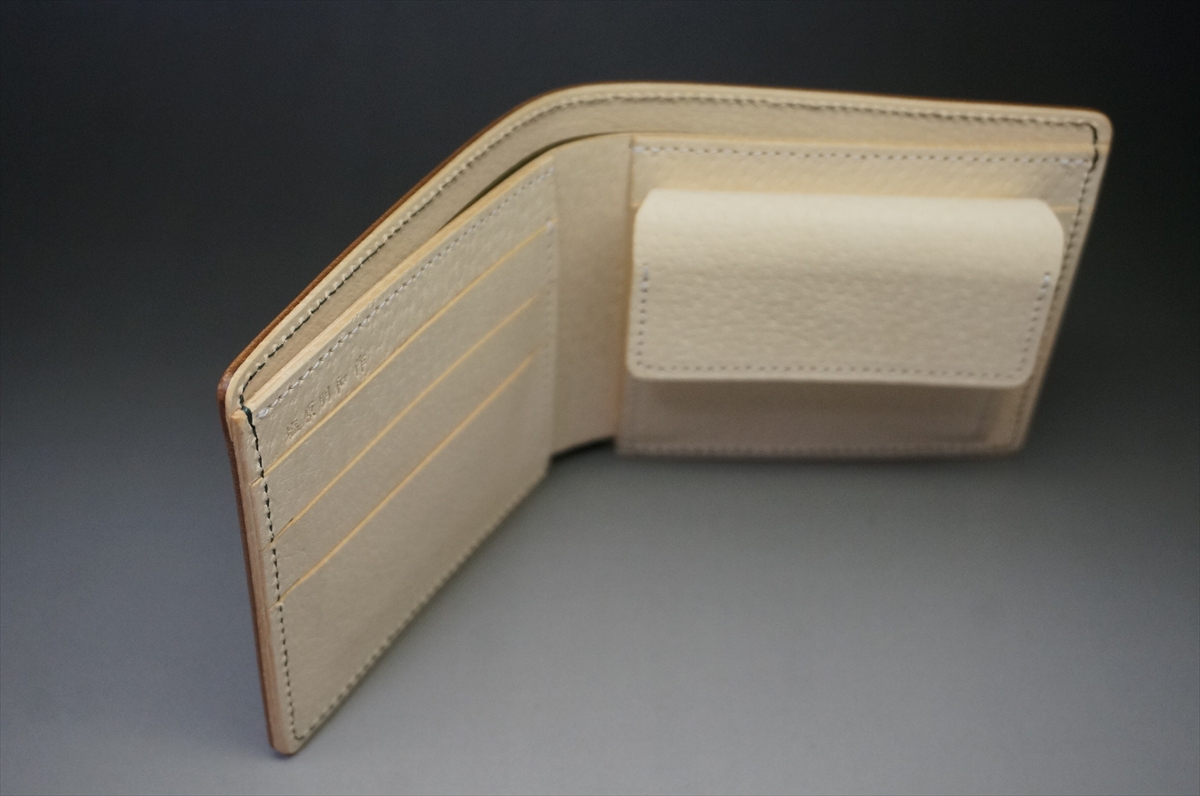 Beige leather bi-fold wallet opened to reveal card slots on the left and a flap pocket on the right.