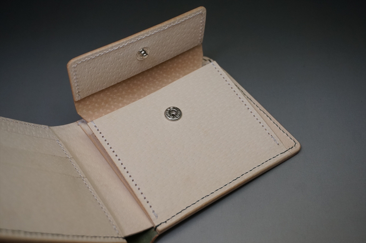 Beige leather wallet opened to show card slots and a snap closure, clean and minimalist design and stitching visible on gray surface.