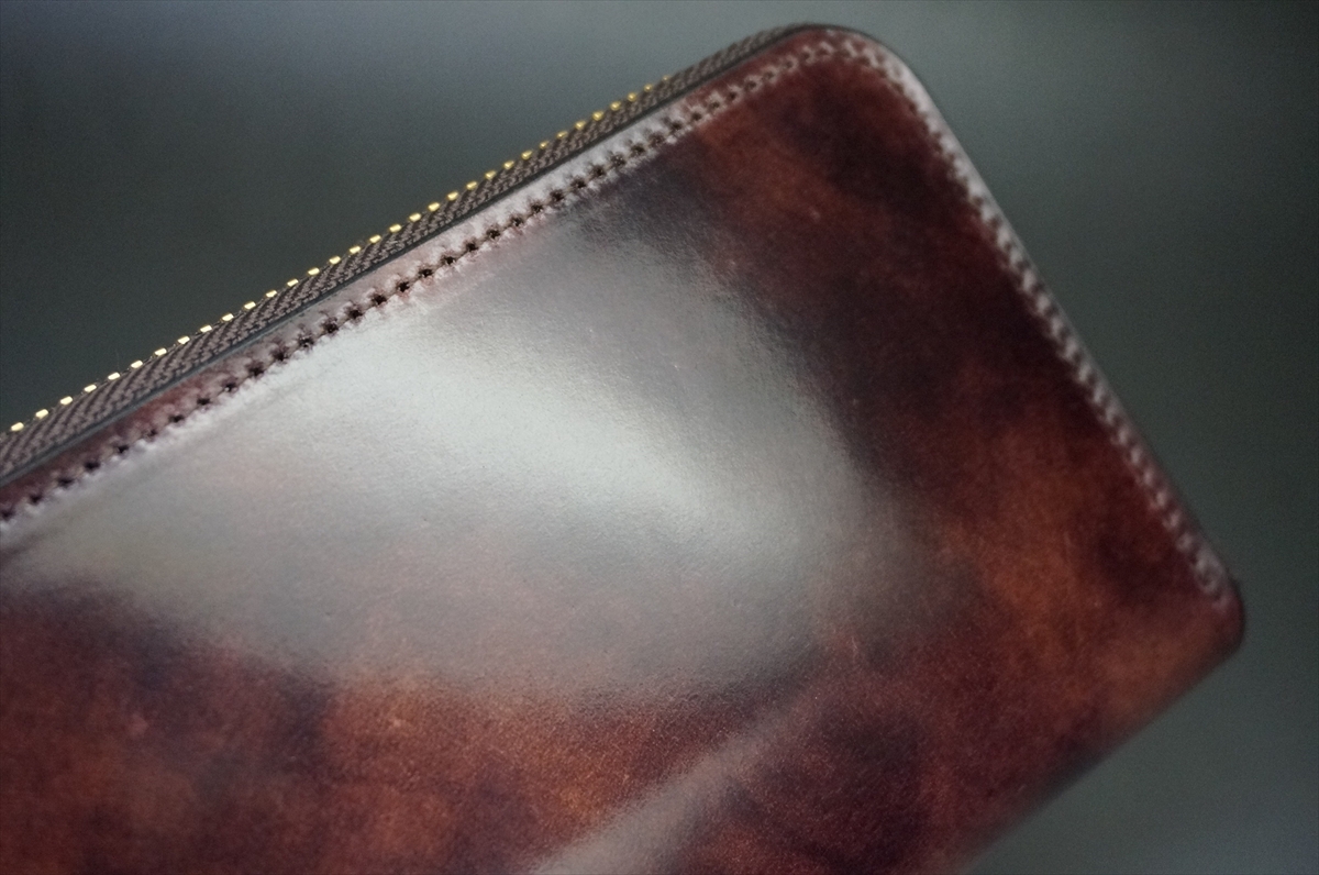 Close-up of a dark brown leather wallet with a gold zipper along the top edge, showing smooth patina and stitching.