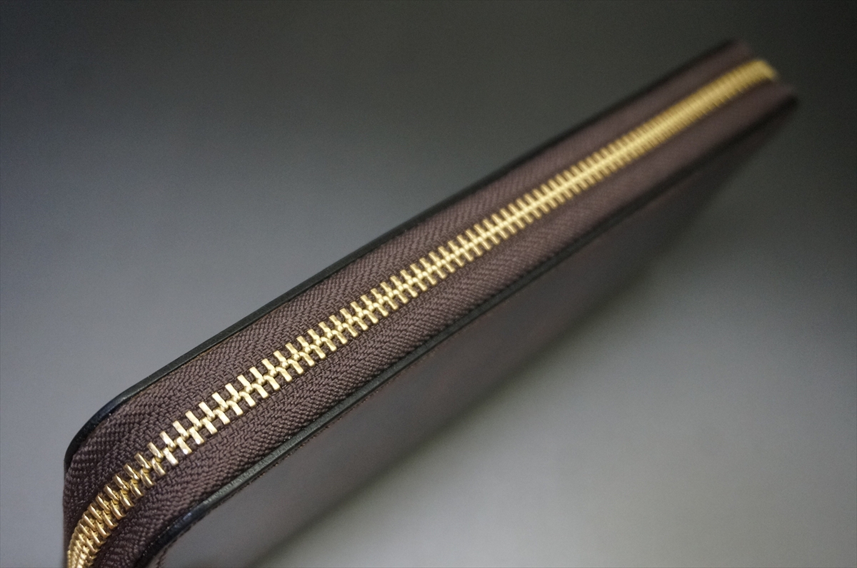 Close-up of a gold zipper along the edge of a brown leather item (wallet/bag).