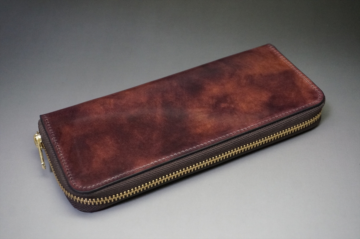Brown leather zippered wallet with a gold zipper resting on a gray background, showing patina marks and stitching details.