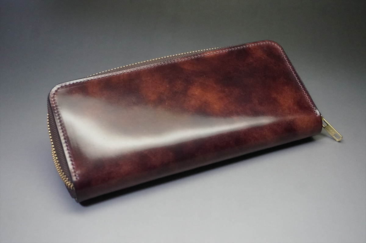 Brown leather zippered wallet resting on a gray surface with a glossy finish and visible stitching around the edges.