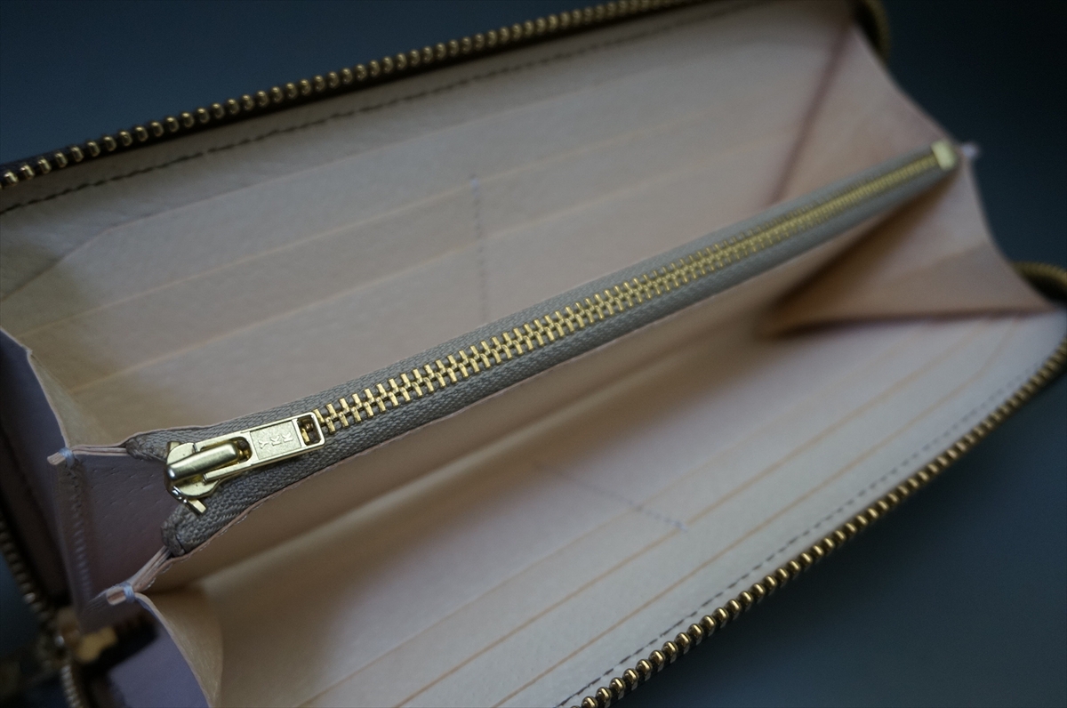 Open beige leather wallet with a gold zipper, showing card slots and empty compartments on a dark surface