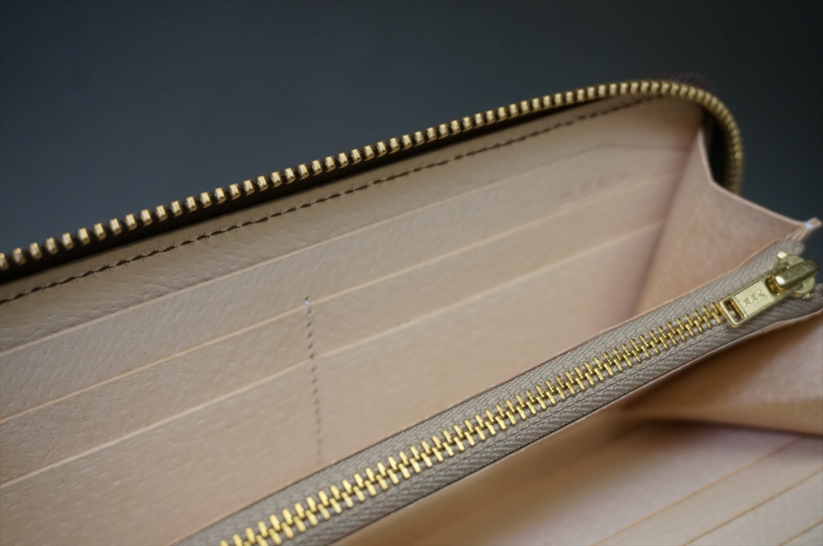 Beige leather wallet opened to show card slots and a gold zipper pocket inside.