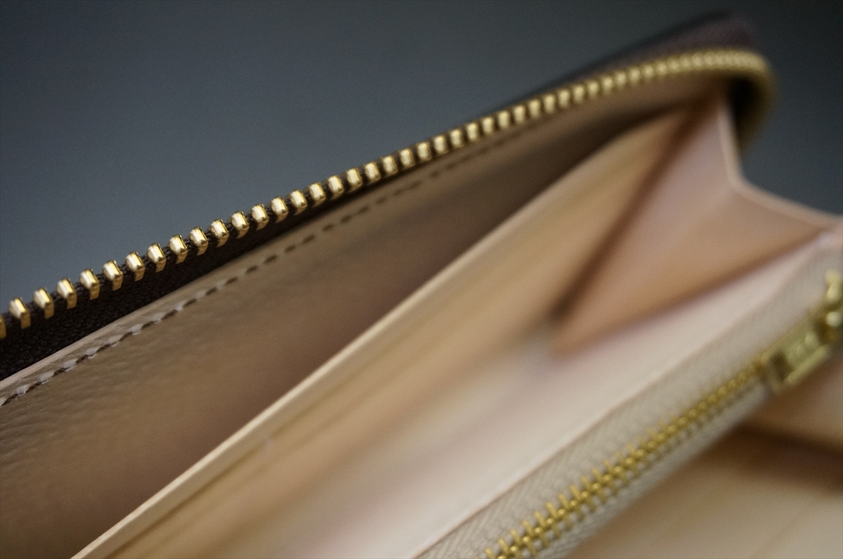Close-up of a beige leather wallet interior with a gold zipper along the top edge.