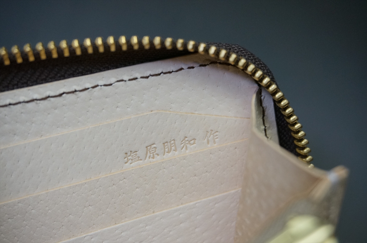 Close-up of a gold zipper along the edge of a white textured leather wallet with embossed Japanese characters inside the seam.