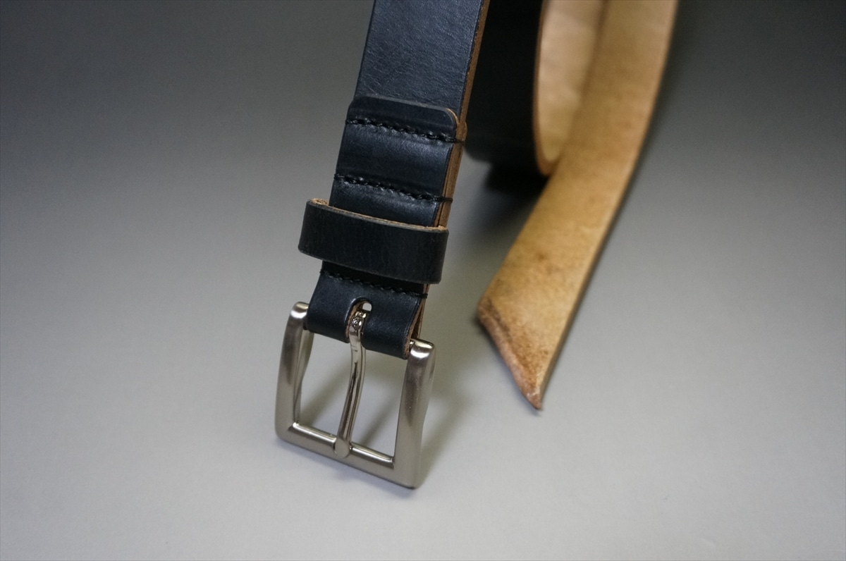 Close-up of a dark blue leather belt with a silver rectangular buckle on a gray surface.