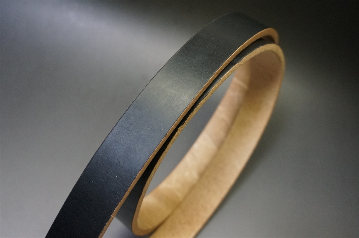 Close-up of a black leather belt strip with a light brown interior edge visible along the curved side.