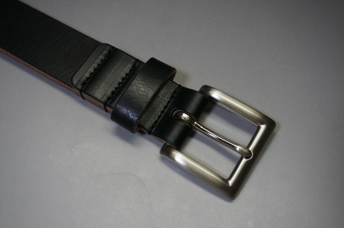 Black leather belt with a silver rectangular buckle on a light gray background.