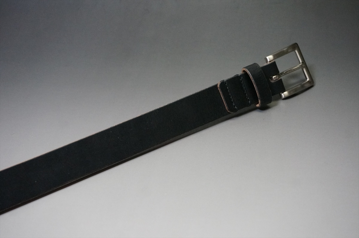 Black leather belt with a silver rectangular buckle resting on a gray gradient background