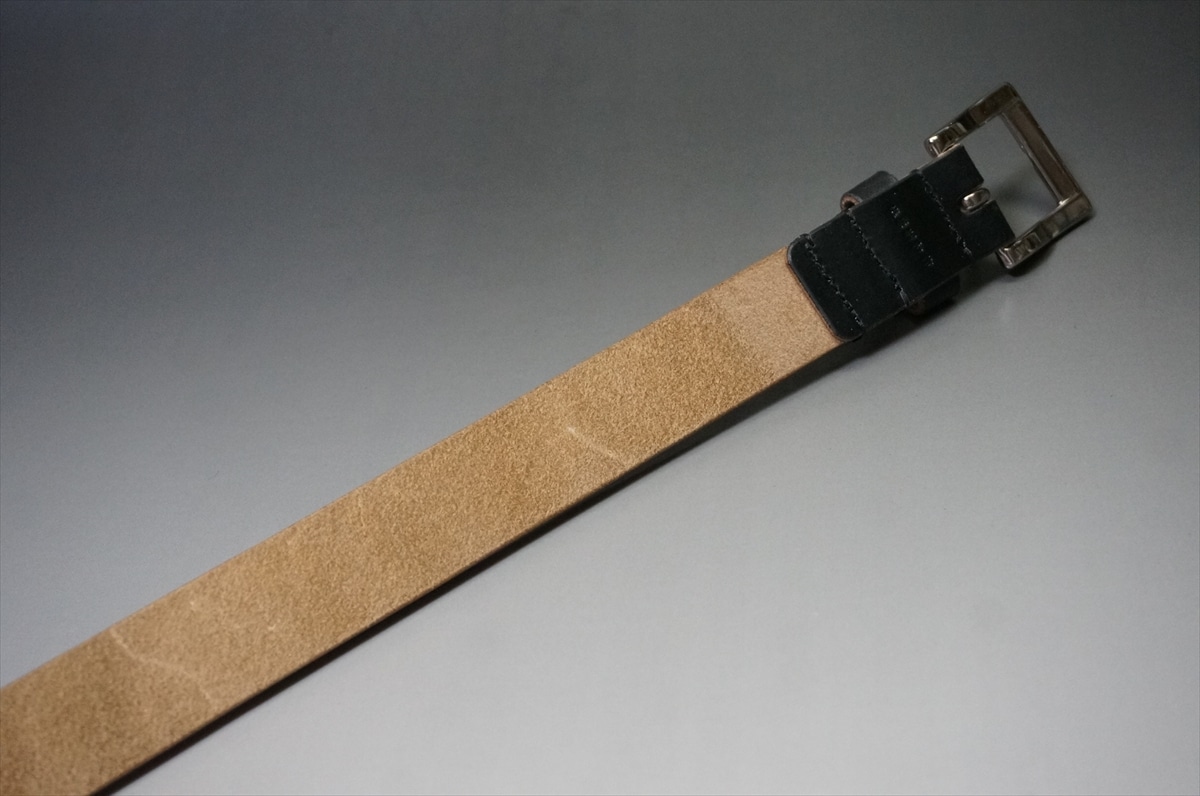 Tan leather belt with a dark stitched leather loop and a metal buckle, laid diagonally on a gray surface.