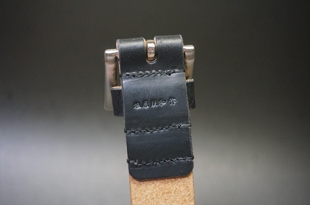 Close-up of a black leather belt end with metal buckle and stitched edges, against a blurred dark background.