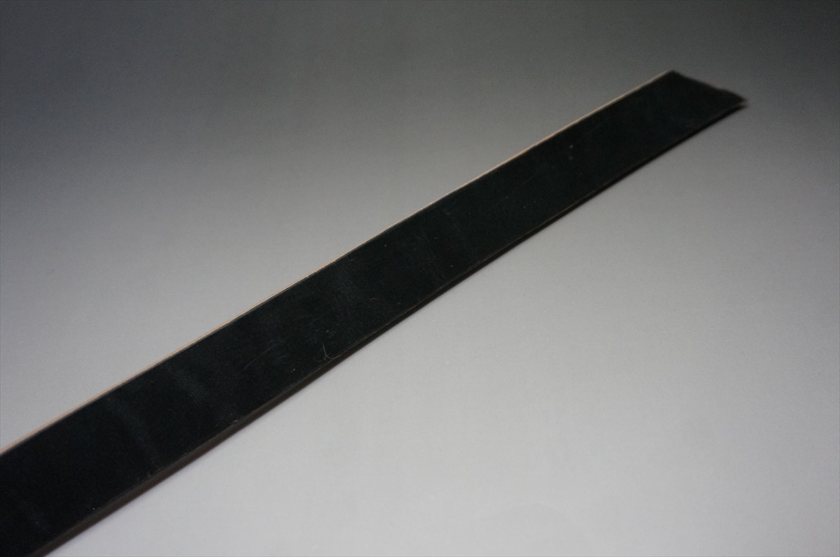 Long black nail file lying diagonally on a light gray surface.