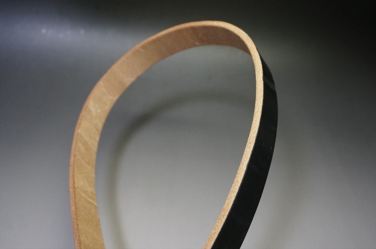 Close-up of a two-tone circular strip: brown cardboard inner edge and glossy black outer edge, forming a loop.
