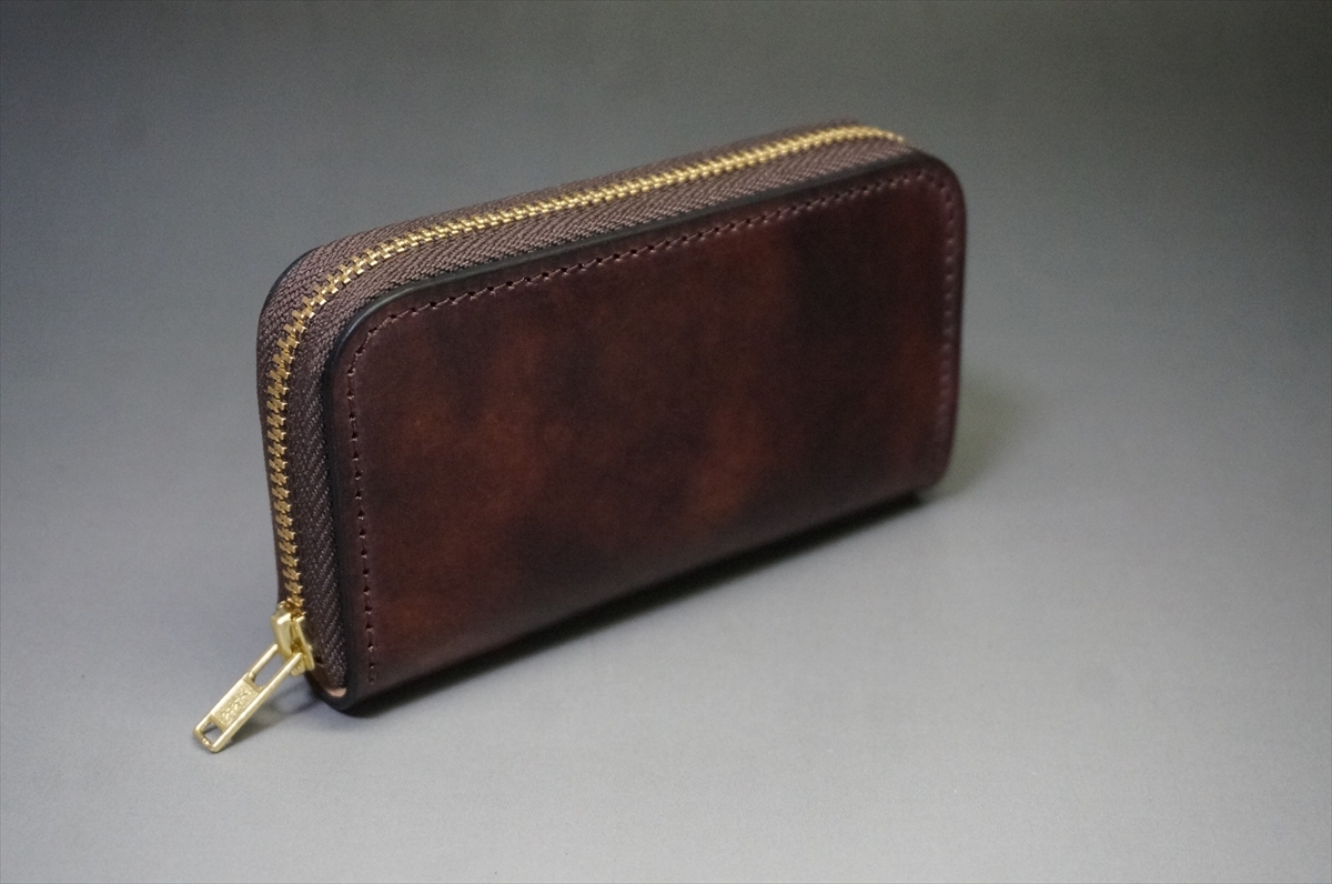 Brown leather zip-around wallet with a gold zipper on a neutral gray surface