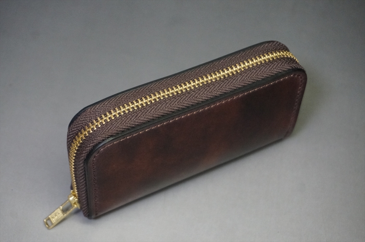Brown leather zippered wallet with a gold zipper along the top edge, closed on a gray surface.