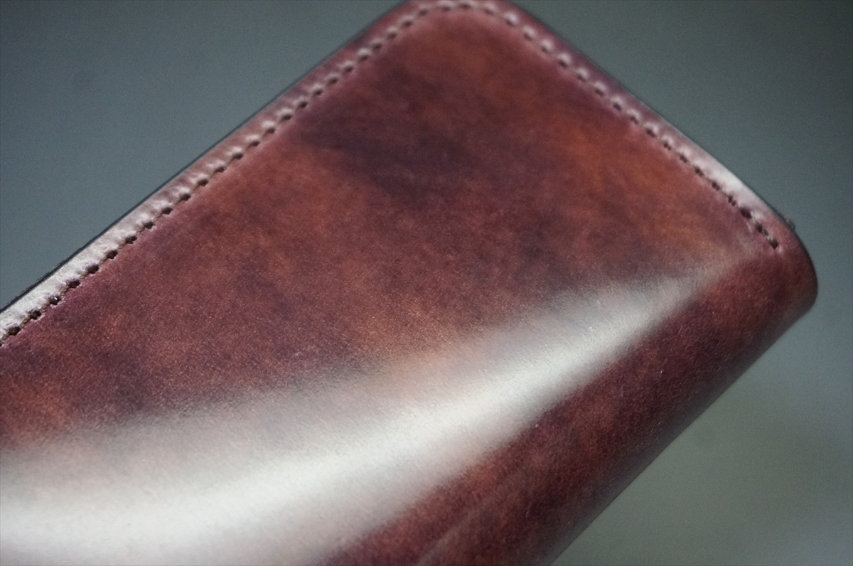 Close-up of a brown leather wallet edge with visible stitching and a smooth, glossy finish.