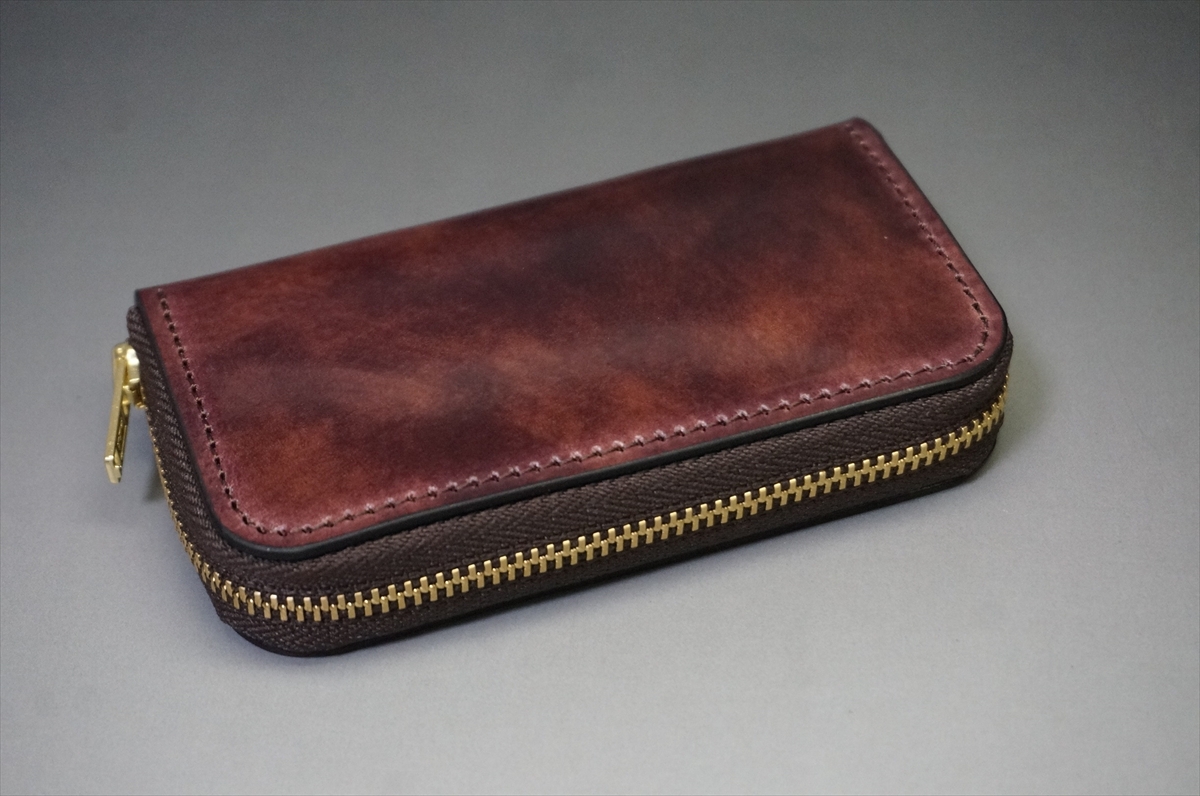 Brown leather wallet with a gold zipper lying on a gray surface.