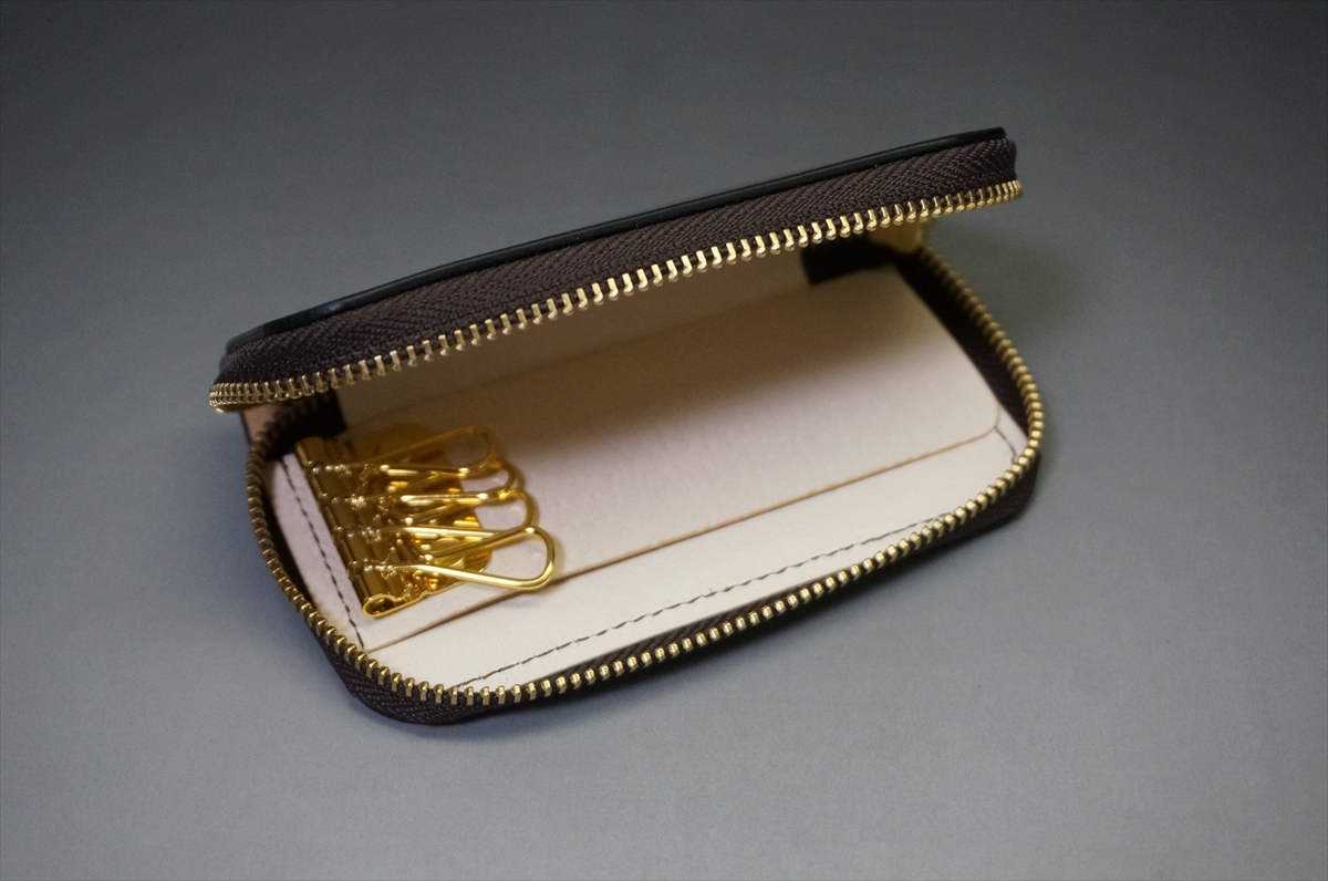 Brown leather zippered key wallet opened to reveal gold-tone key hooks on a light interior.